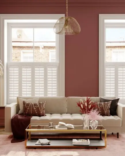 White cafe style shutters in dusty warm red living room with cream couch and gold furnishings