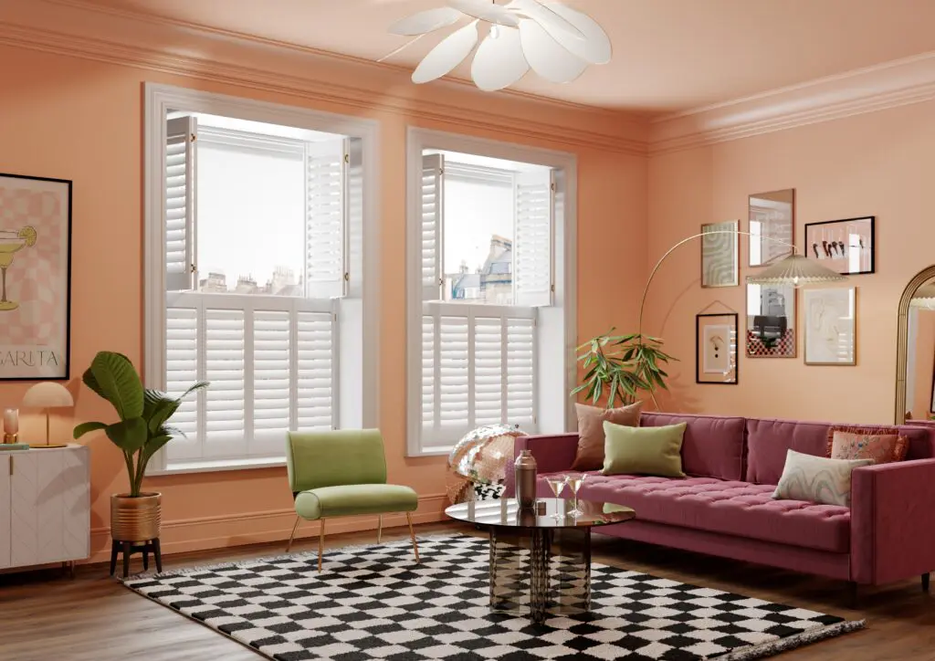 White tier on tier shutters with top panels open in living room with pink sofa, green chair and checked rug