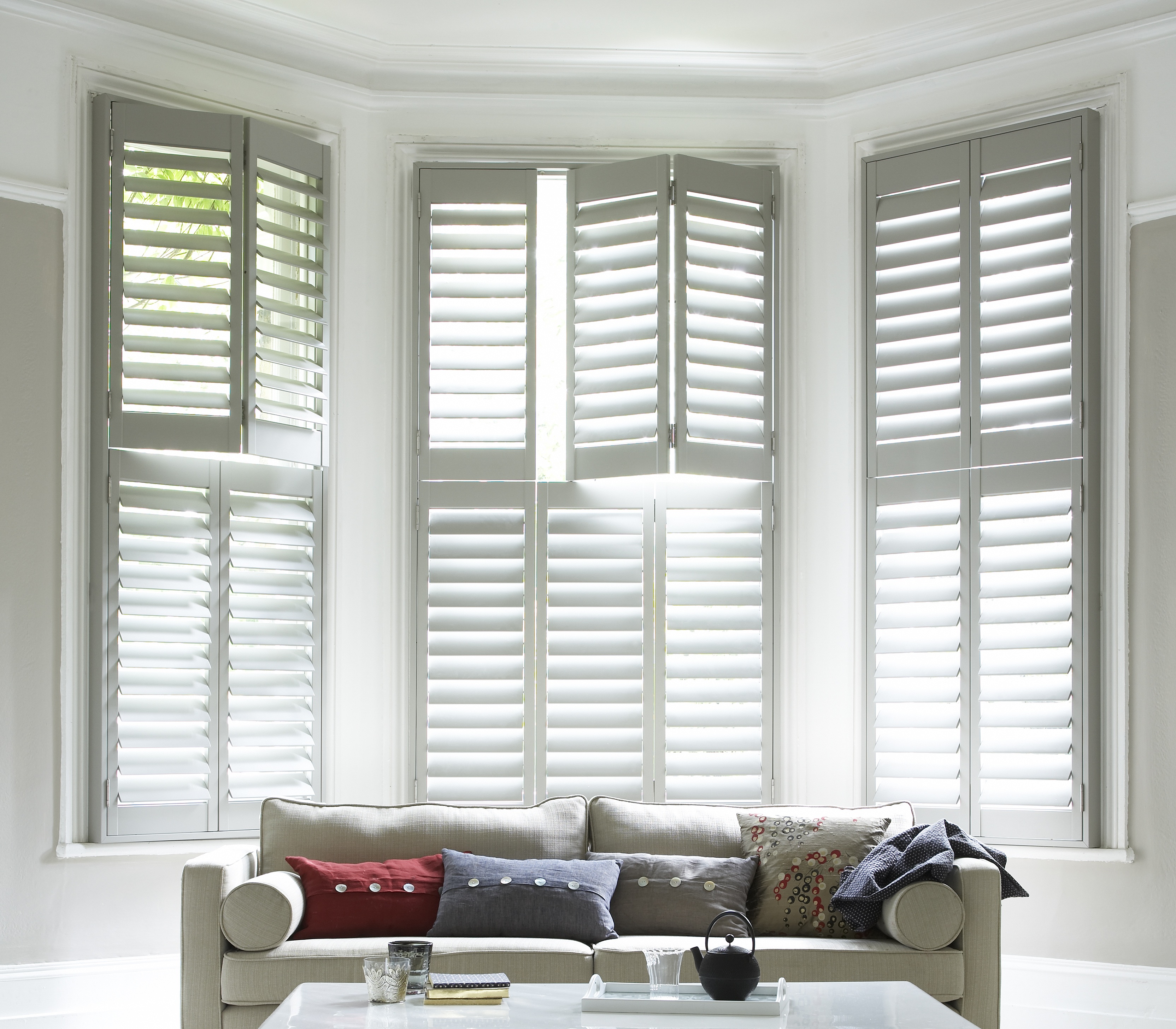 White Tier on tier shell shutters in the living room with grey sofa