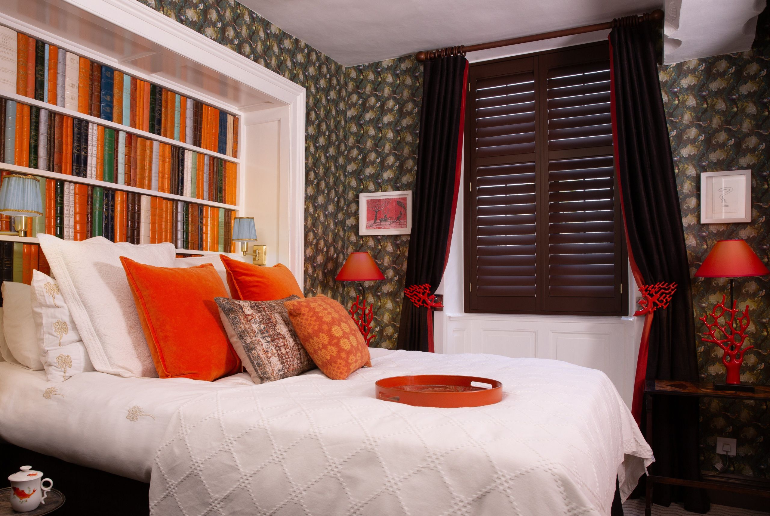 dark shutters paired with long curtains of the same colour in a bedroom with double bed with book case behind