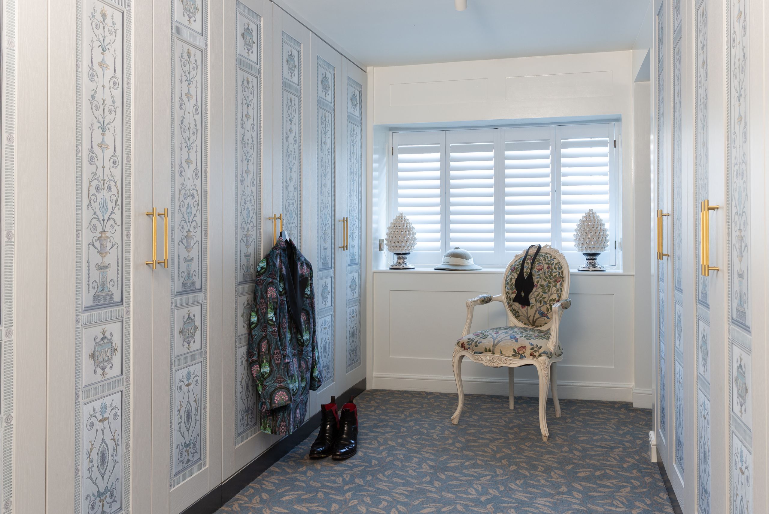 light blue shutters with long wardrobe doors with patterns on the door panels and a chair in front of the window